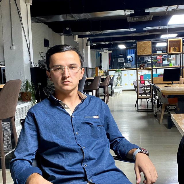 Portrait of Yusufjon Axmedov seated in a studio workspace.